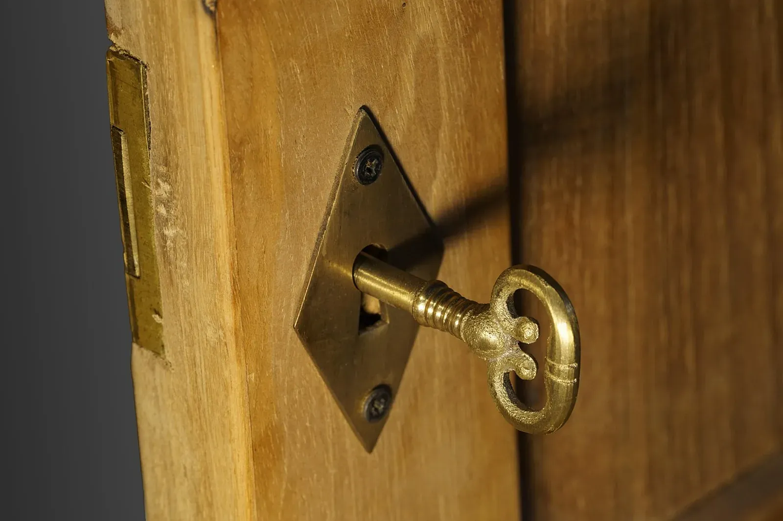 Ornate brass key left in a diamond-shaped keyhole plate on a natural wood door