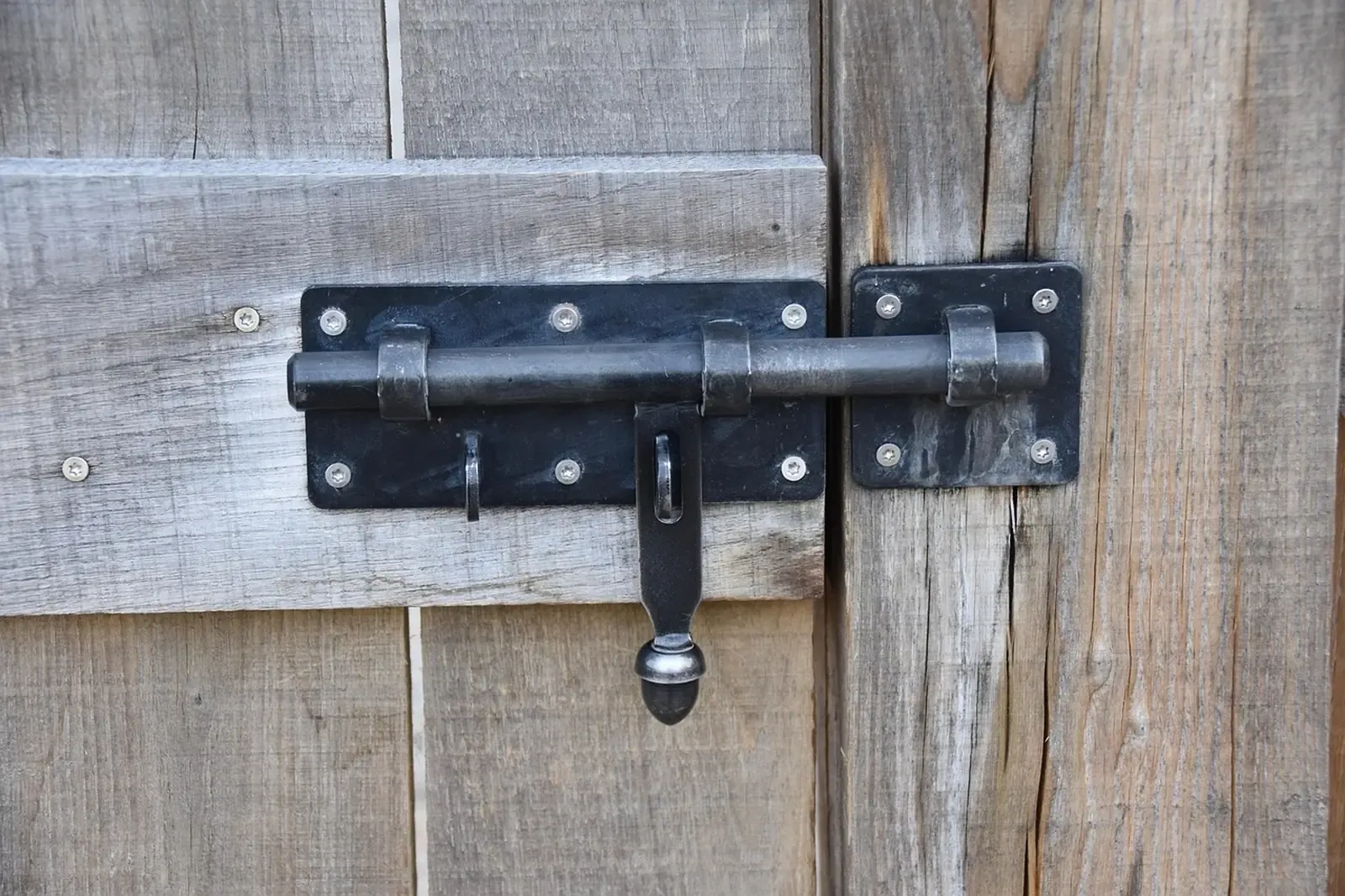 Black iron slide bolt and hasp mounted on gray weathered wooden planks