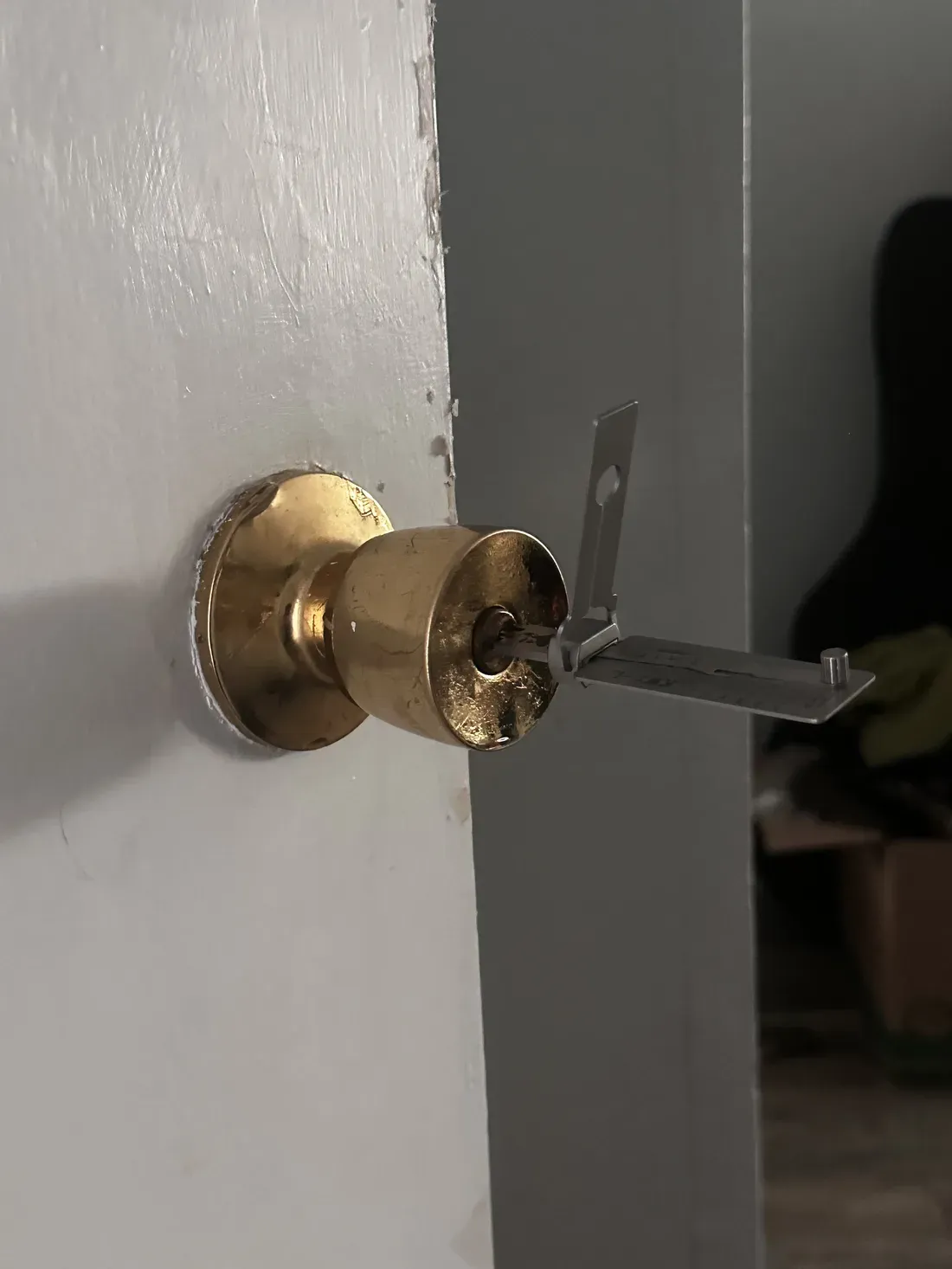 A brass door knob on a white door with a thin metal tool set into the lock