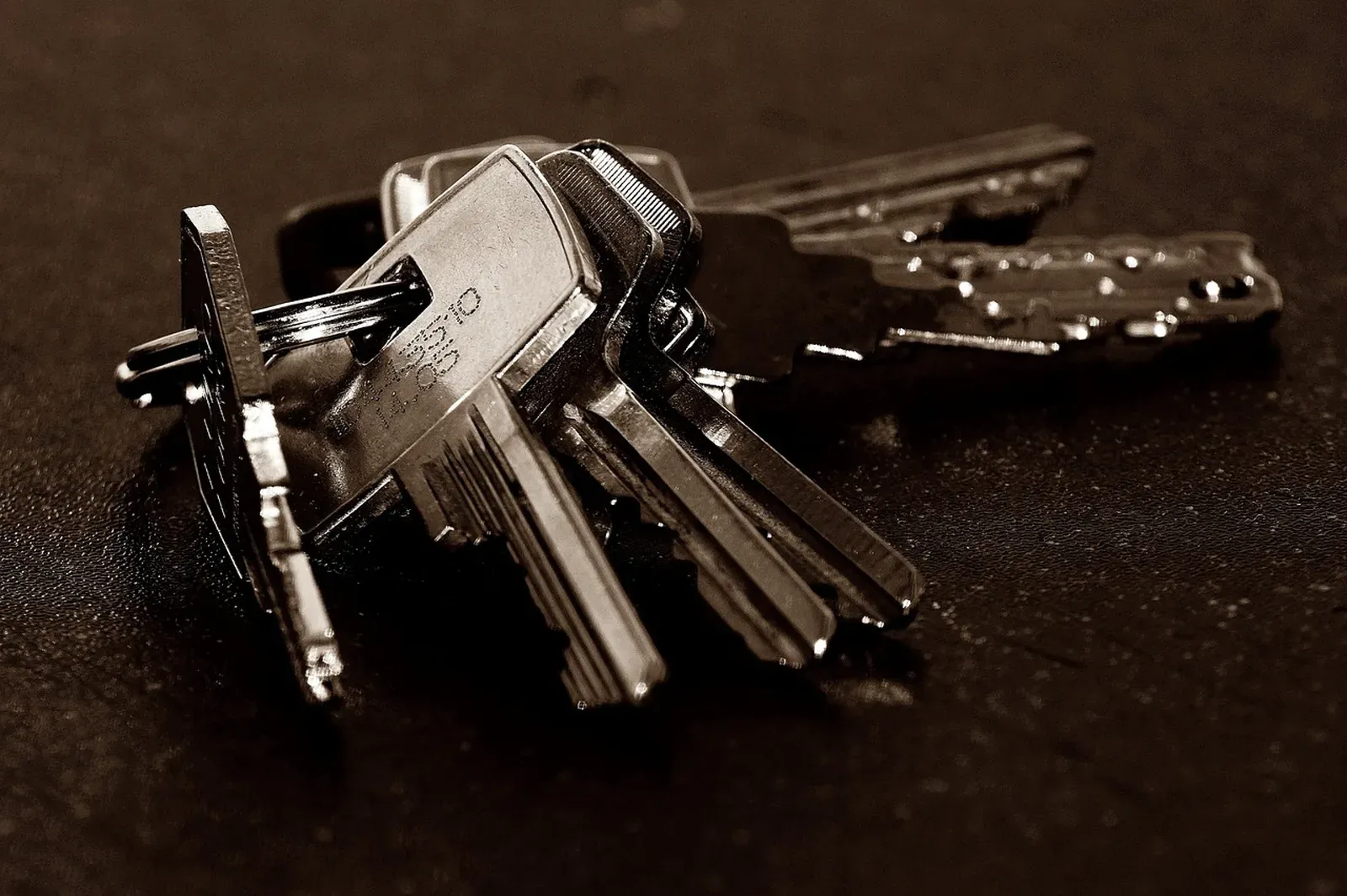 A bunch of metal keys on a ring resting on a dark surface in moody sepia tones