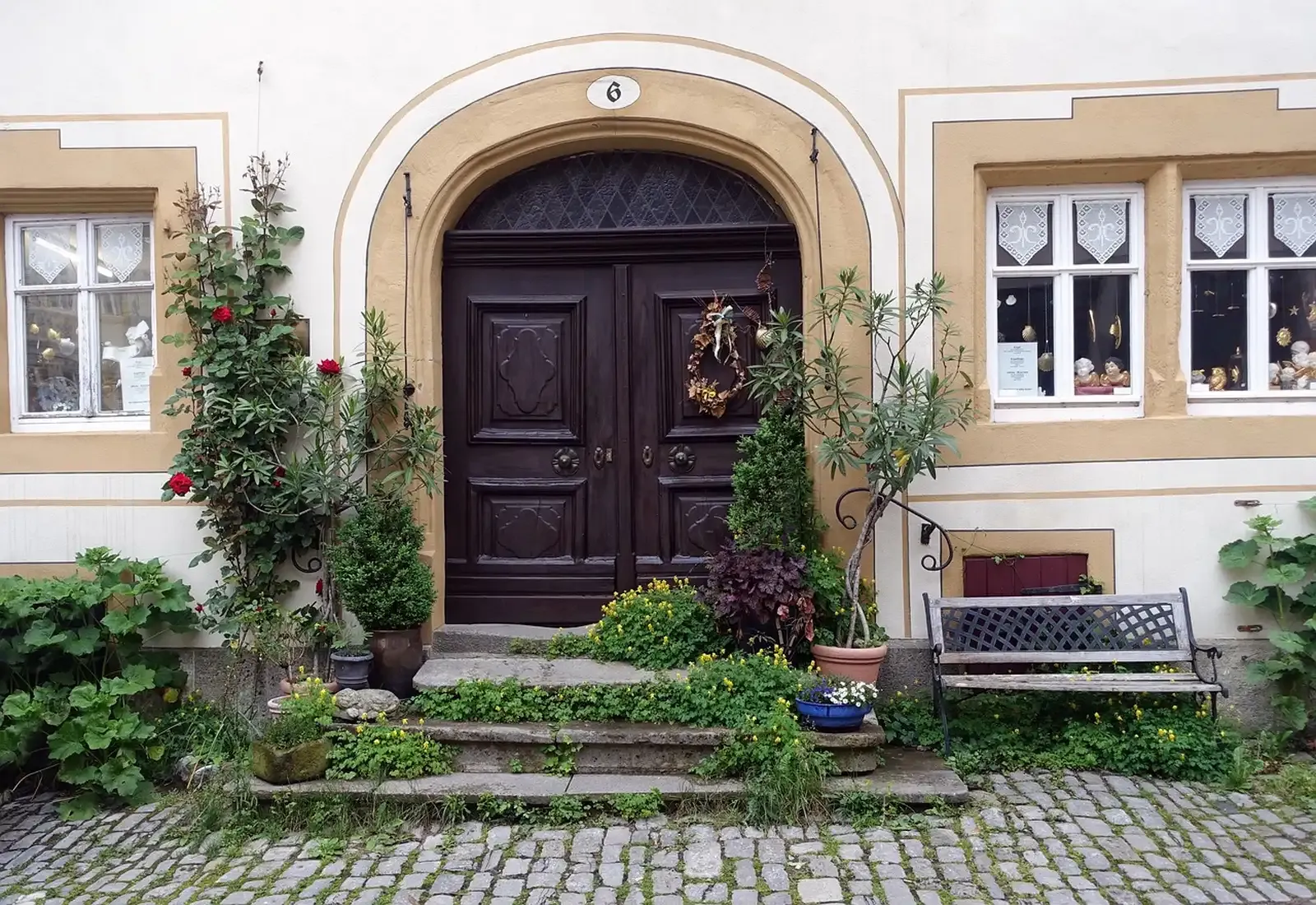 A carved dark wooden double front door framed by an arch, stone steps, climbing roses and potted plants