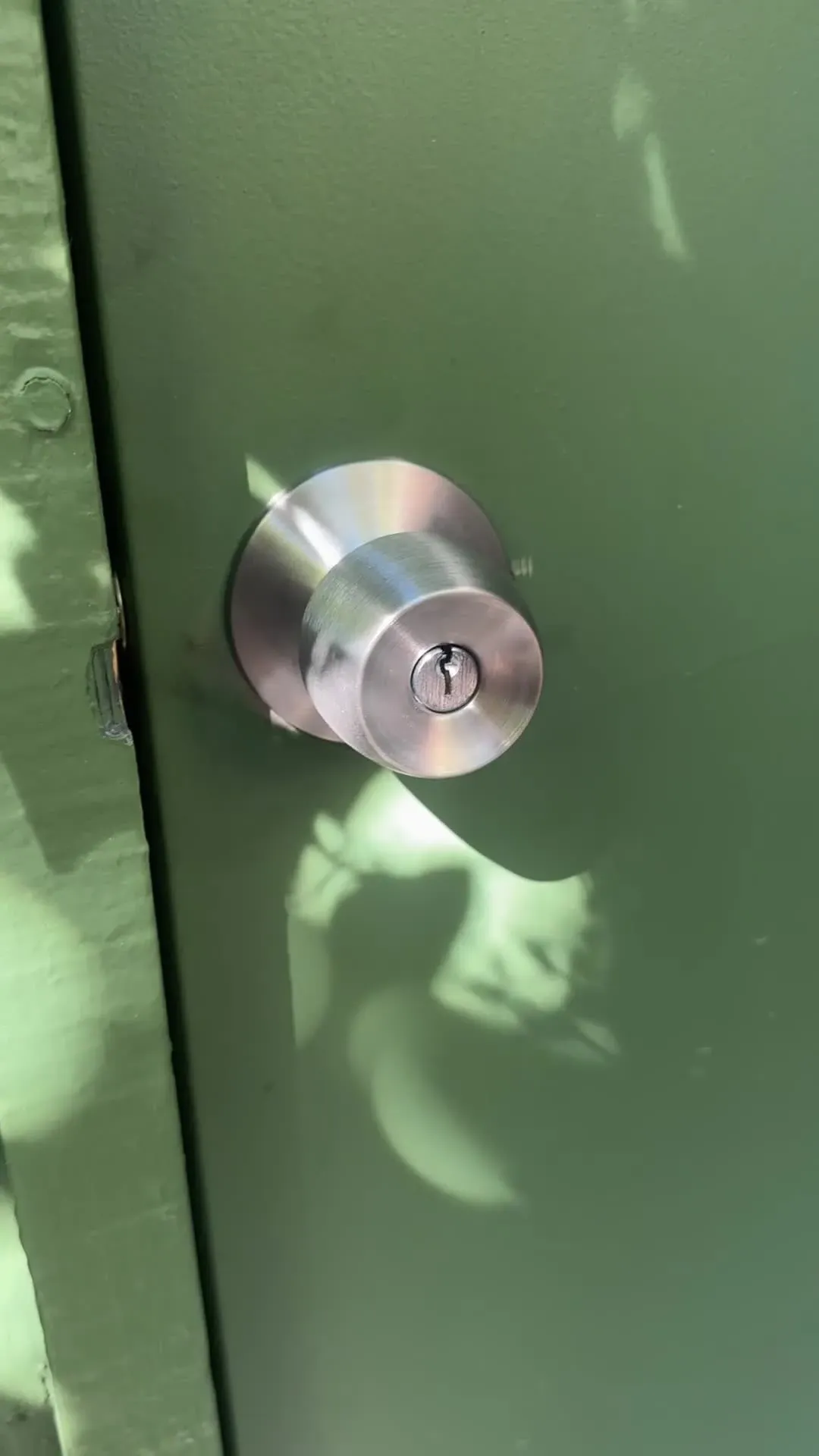 Close-up of a stainless steel keyed door knob on a green door