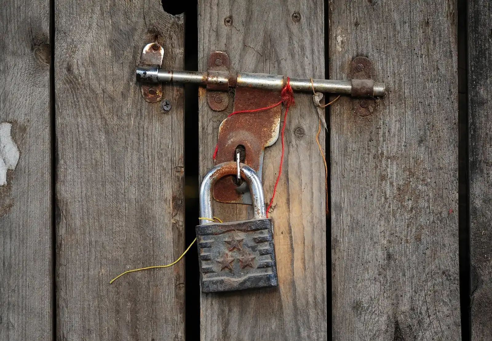 Weathered wooden plank gate with a sliding bolt latch and a heavy rusted padlock