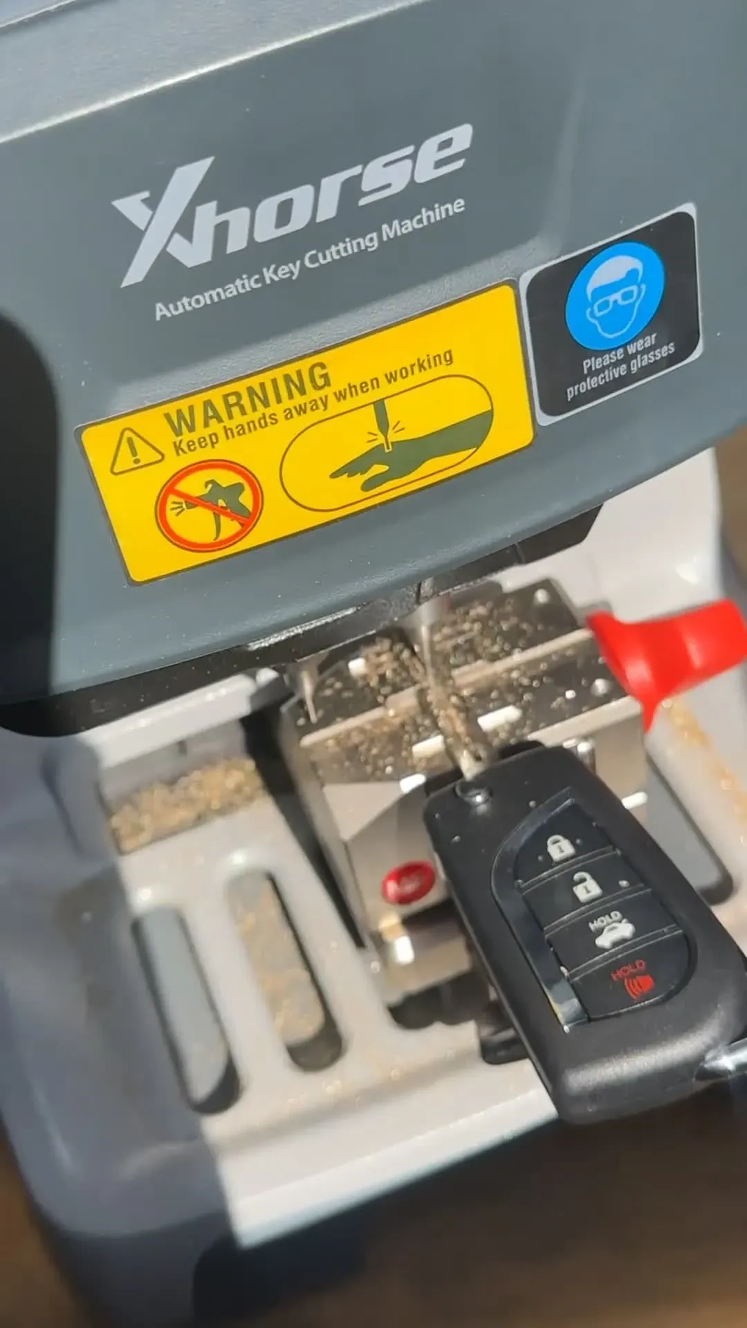 A key cutting machine on a workbench with a black key fob clamped in the jaws