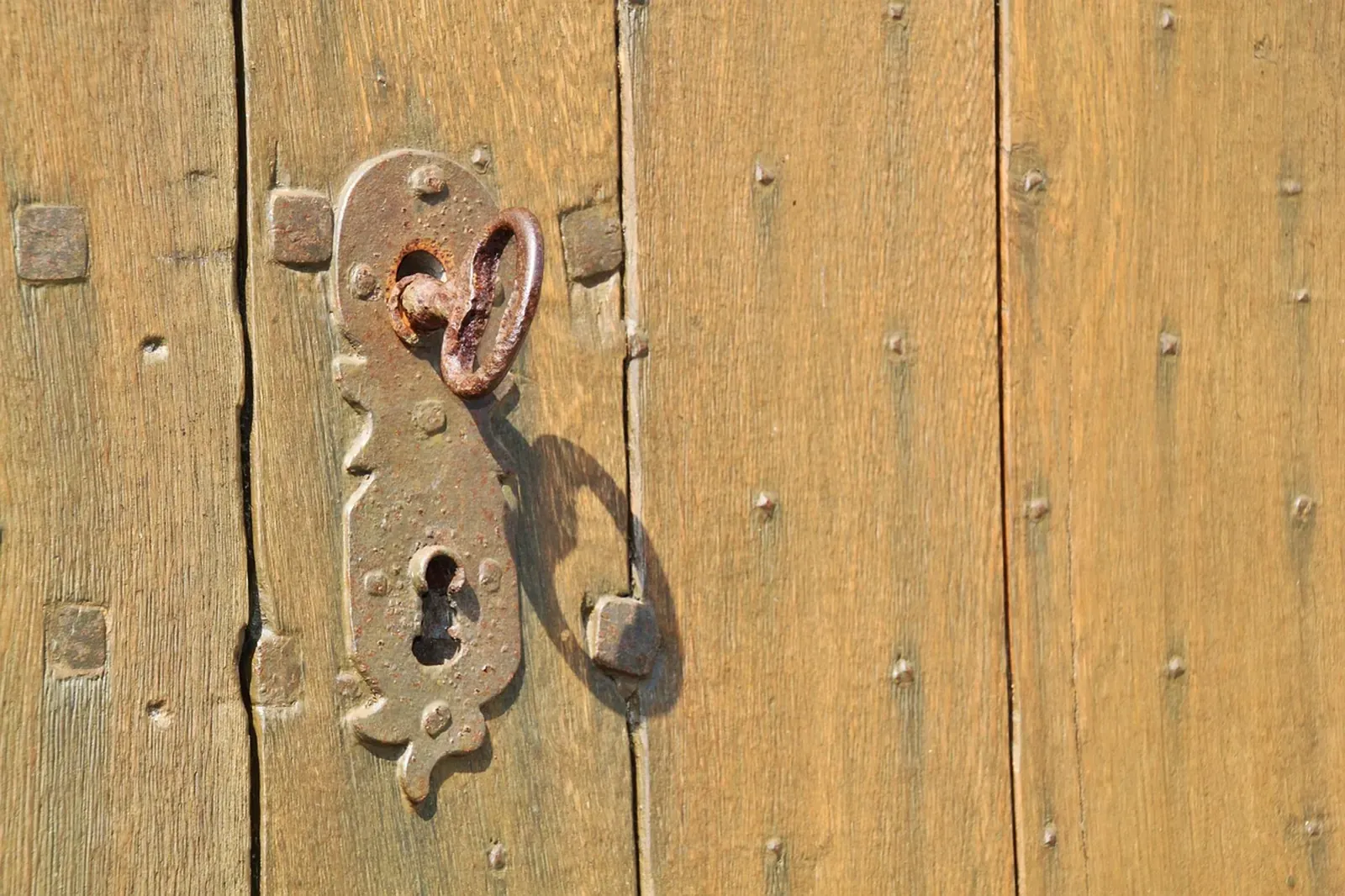 Rusty iron key sitting in the ornate escutcheon of a studded old wooden door