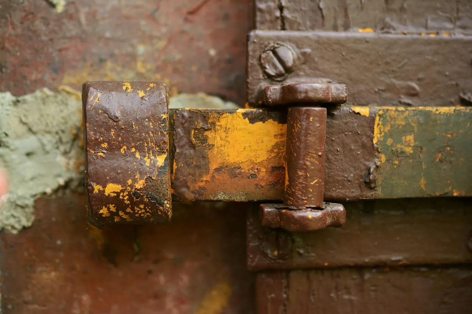 Rust-streaked iron door latch and hasp with peeling brown paint on an old wooden door