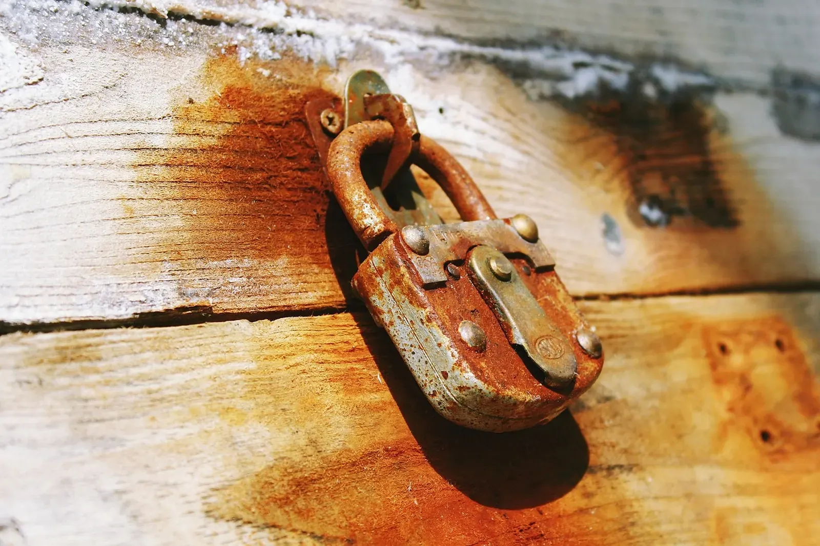 Heavily rusted padlock hanging from a hasp on a sun-bleached wooden door