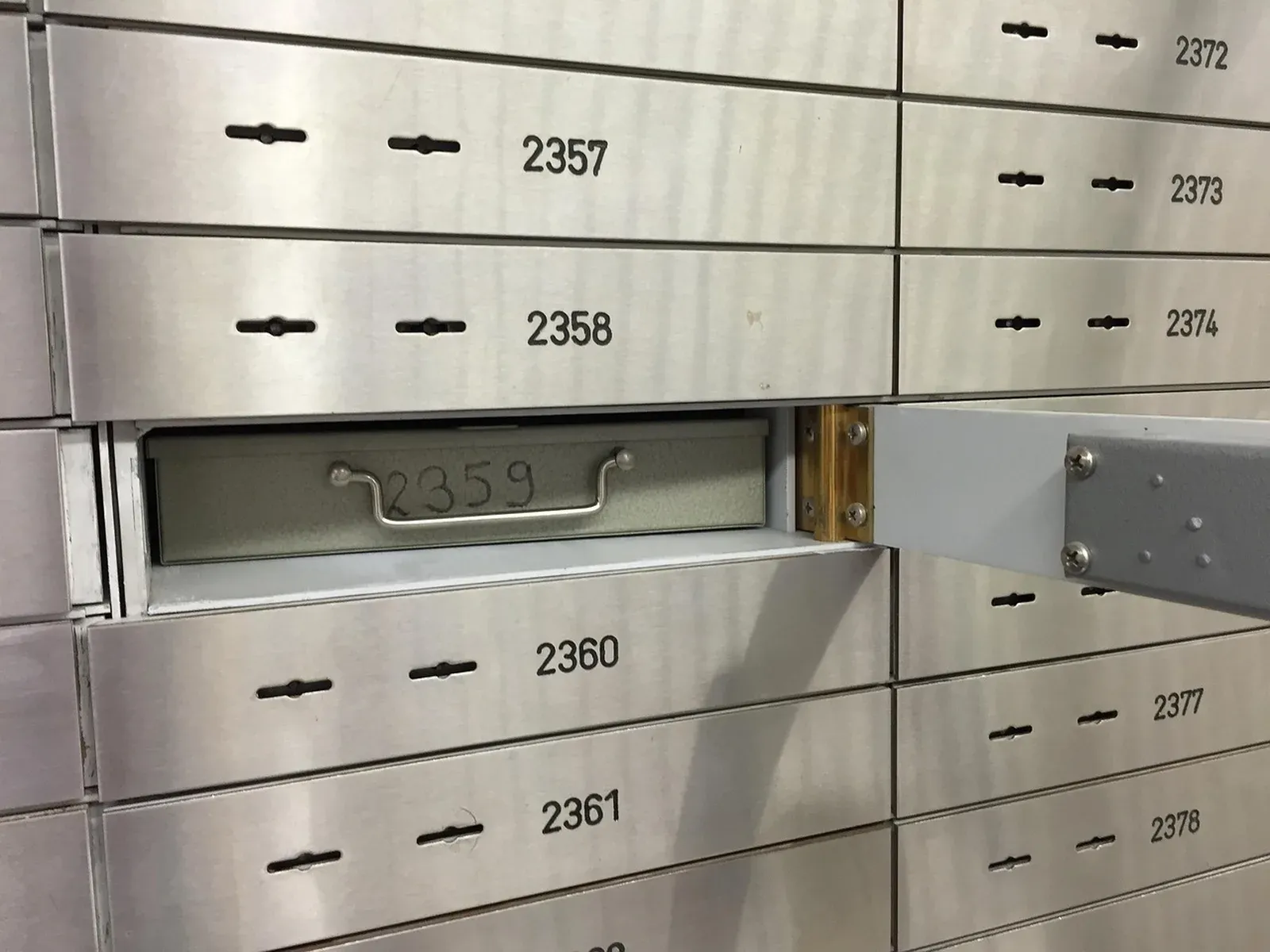 Rows of numbered steel safe deposit boxes with keyholes, one drawer pulled open to show its metal box