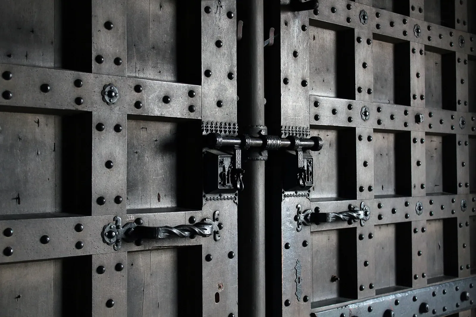 Dark studded wooden double door with a wrought iron sliding bolt and twisted iron handles